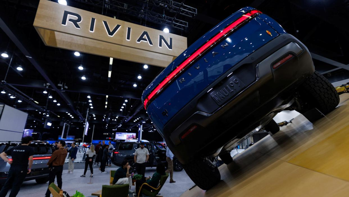 Rivian electric truck displayed on an angled platform at an auto event with visitors nearby