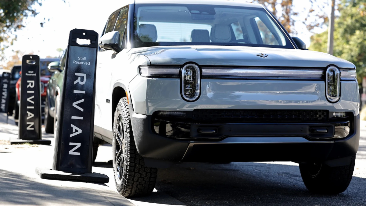 Rivian electric truck parked beside branded charging stalls in outdoor setting.